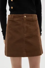 Falda mini de corte recto confeccionada en pana de algodón color marrón, con cierre de botón frontal y trabillas para cinturón.