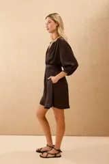 Vestido corto de color negro, con mangas tres cuartos, cuello mao y cierre frontal con botones. Incluye un lazo a tono para ajustar en la cintura y bolsillos laterales.