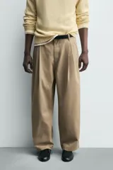 Pantalón chino de corte wide fit confeccionado en tejido de algodón. Presenta pliegues frontales, bolsillos laterales y bolsillos traseros de vivo, con cierre frontal de cremallera y botón.