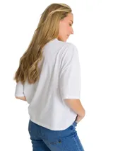 Remera blanca de corte oversize con cuello redondo y mangas cortas. Presenta un estampado gráfico en el pecho con el logo de la marca y una palmera en color salmón.
