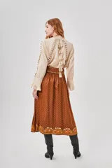 Falda larga marrón con estampado central de motivos florales en tonos naranjas y blancos, y pequeños puntos blancos distribuidos por toda la tela.