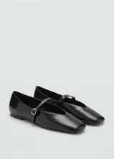 Zapato tipo bailarina de efecto charol color negro, con punta redonda y tira fina en el empeine que cuenta con una hebilla decorativa efecto joya.