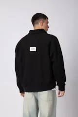 Buzo de cuello alto con cierre frontal parcial, manga larga y diseño holgado. Presenta un pequeño logo bordado en el pecho.