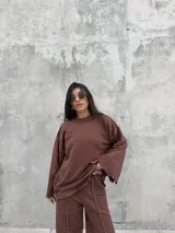 Buzo oversize de color marrón chocolate, con cuello redondo, mangas anchas y diseño con costuras expuestas en contraste. Presenta terminaciones desflecadas en el ruedo y en los puños.
