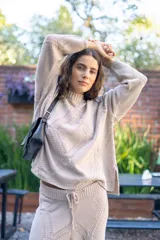 Sweater tejido de punto color beige con diseño geométrico de rombos en relieve. Presenta cuello redondo a la base, mangas largas y silueta amplia con aberturas laterales en el ruedo.