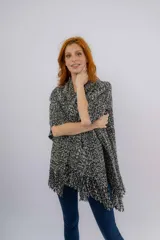 Ruana artesanal tejida en telar manual, con diseño jaspeado en tonos negro y crudo. Presenta una textura rústica y terminación con flecos en el ruedo, además de una etiqueta de cuero con la marca Pura Lana.
