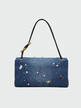 Bolso de hombro rectangular de denim azul, con solapa frontal decorada con múltiples charms metálicos y de esmalte, incluyendo cerezas, lazos, estrellas y candados. El bolso tiene herrajes dorados y correa de hombro de cuero negro.