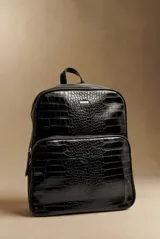 Mochila de gran tamaño con diseño de textura croco, confeccionada en cuero vegano color negro. Cuenta con un compartimento principal con cierre, un bolsillo frontal amplio y una manija superior.