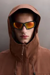 Cazadora deportiva color marrón confeccionada en tejido técnico de tres capas con membrana impermeable. Cuenta con cuello alto con capucha ajustable, mangas largas con puños reforzados ajustables, aberturas con cremallera en axilas, bolsillos frontales con cremallera y bajo ajustable con elásticos laterales.