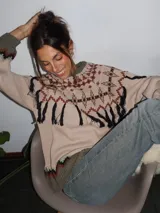 Sweater tejido con técnica intarsia, de silueta holgada y cuello a la base. Presenta un diseño con motivos geométricos, detalles de flecos colgantes y terminaciones en tejido acanalado en color rojo en puños y ruedo.