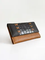 Billetera de cuero combinada en color negro y camel, con diseño de solapa con textura de cocodrilo y detalles de costuras en forma de X. Cuenta con cierre de broche y monedero externo.