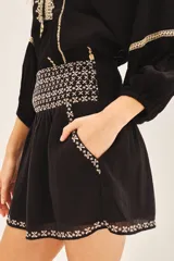 Falda corta blanca de algodón con bordados negros en el frente y el ruedo. Presenta un detalle de punto smock en la cintura trasera.