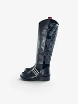 Bota de caña alta en cuero negro con punta redonda y taco bajo. Presenta un panel lateral de gamuza con bordado geométrico en hilo gris, herraje metálico decorativo en el empeine y cierre interno. El diseño cuenta con una boca asimétrica y forro interior de cuero.