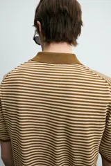 Polo de punto de algodón con corte regular fit, manga corta y cuello solapa con abertura frontal en forma de V. Presenta un diseño a rayas horizontales marrones y beige, con ribetes en color marrón oscuro en el cuello, puños y bajo.