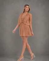 Vestido corto de gasa color durazno, con escote en V, drapeados en el frente y detalle de cadena dorada. Presenta mangas cortas tipo capa y cintura elástica con falda fluida.