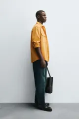 Camisa de hombre color mostaza, con cuello solapa, manga larga y dos bolsillos plastrón con solapa en el pecho. Presenta un calce relajado y cierre frontal de botonadura.