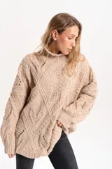 Sweater de tejido de punto grueso en color beige, con cuello alto y diseño de trenzas y calados en toda la prenda. Presenta un corte holgado y mangas largas con puños acanalados.