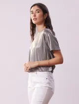Blusa gris metalizada de tejido lurex, marca June & Hudson, con cuello redondo y ruedo con nudo en la espalda.