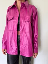 Camisa magenta de cuero sintético, de corte recto, con cuello clásico, cierre frontal con botones a presión, dos bolsillos de parche con solapa en el pecho y mangas largas con puños abotonados.