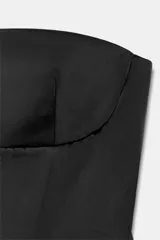 Top negro de tejido satinado, sin tirantes y con escote recto. Presenta costuras marcadas y diseño con peplum en la parte inferior, con cierre de cremallera oculta en la espalda.