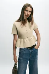 Chaqueta de punto color beige claro, con cuello redondo, manga corta y bajo peplum con pliegues. Cierre frontal con botones forrados a tono.