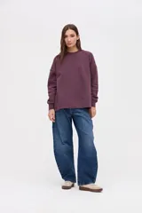 Buzo oversize de felpa con friza, color bordó, con cuello redondo, mangas largas con cortes decorativos y tajos laterales en el ruedo. Presenta un bordado de la marca en una de las mangas.