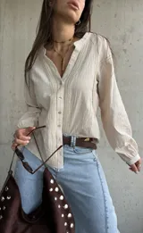 Camisa de manga larga color beige con diseño abotonado frontal, cuello mao y detalles de bordados y encaje en el frente y las mangas.