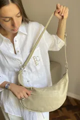 Cartera bandolera de cuero negro con diseño de media luna, decorada con tachas metálicas plateadas. Cuenta con correa regulable, cierre principal y bolsillo interior con forro.