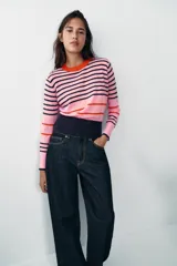 Jersey de punto de cuello redondo y manga larga con puños ajustados. Presenta un diseño de rayas horizontales en tonos rosa, azul marino y detalles en rojo.
