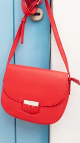Bandolera de cuero sintético color rojo, con diseño de tapa frontal y detalle de broche metálico rectangular. Incluye correa larga ajustable para llevar al hombro o cruzada.