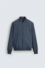 Cazadora tipo bomber ligera confeccionada en tejido técnico, con cierre frontal de cremallera, cuello, puños y bajo en rib elástico, y bolsillos laterales de vivo.