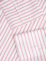 Camisa de popelín de manga larga con cuello clásico y cierre frontal de botones. Presenta un diseño de rayas verticales finas en color rosado sobre fondo blanco, con un corte relajado y puños anchos.