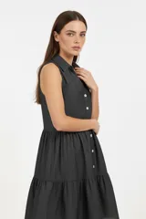 Vestido midi de algodón color gris oscuro, con cuello camisero, sin mangas y cierre frontal con botones. Presenta un diseño holgado con falda de volados escalonados.