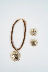 Set compuesto por un collar de cordón trenzado color marrón con dije central en forma de sol dorado y un par de aros a juego con el mismo diseño de sol.
