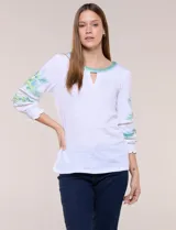 Blusa blanca de silueta semi entallada, confeccionada en tejido texturado. Cuenta con escote en V con abertura y vivo bordado multicolor, mangas 3/4 abullonadas con bordados, calados y puños elásticos.