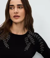 Suéter de punto en color negro con cuello redondo y mangas largas. Presenta un delicado bordado floral con pedrería en la zona de los hombros.