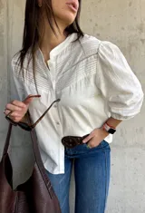 Camisa blanca de estilo romántico con cuello mao, botones frontales y mangas tres cuartos abullonadas con detalle de frunces. Presenta un diseño con textura sutil y costuras decorativas en la parte superior delantera.