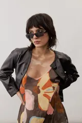 Chaqueta de cuero negra con cuello redondo, cierre frontal de botones forrados y bolsillos ribeteados con detalles de costura decorativa.