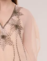 Vestido estilo túnica de dos piezas, color salmón, compuesto por un sobrevestido holgado de gasa semitranslúcida con mangas kimono y escote en V con bordados brillantes de piedras y cuentas, y un vestido base interior tipo enagua de tirantes finos.