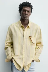 Camisa de corte regular fit de tejido de algodón, con diseño de rayas verticales amarillas y azules. Cuenta con cuello abotonado, manga larga con puños abotonados, un bolsillo aplicado en el pecho y cierre frontal con botones.