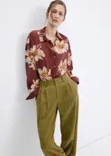 Camisa de manga larga color marrón con estampado floral grande en tonos beige y blanco, cuello camisero y cierre frontal con botones.