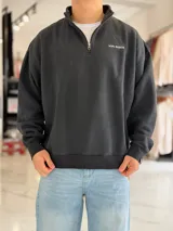 Buzo negro de cuello alto con medio cierre y diseño oversize, con pequeño estampado de texto blanco en el pecho.