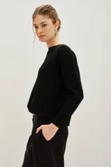 Sweater negro de punto con cuello redondo, manga larga y detalle de tachas metálicas en los hombros formando un diseño de rayo.