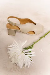 Sandalia color beige de cuero vacuno, con tiras anchas cruzadas y detalle de nudo central. Tiene pulsera regulable en el talón, taco ancho de 5,5 cm y suela sintética.