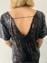 Vestido corto negro de lentejuelas con escote en V, mangas cortas y flecos en el ruedo.