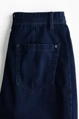 Jean de denim rígido azul oscuro, con corte holgado y diseño curvo en las piernas. Presenta cintura estándar con cordón ajustable, cierre con botón y bolsillos clásicos.