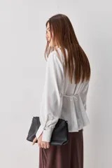 Camisa blanca de manga larga con textura suave y caída liviana, cuello camisero, puños anchos y fruncidos sutiles en los hombros.