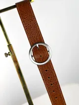 Cinturón de cuero con textura de reptil en color marrón, con hebilla circular metálica en tono dorado envejecido.