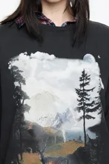 Camiseta negra de corte oversize con cuello redondo y mangas cortas. Presenta un estampado gráfico grande en el frente que simula un paisaje nocturno o crepuscular con un ciervo, árboles y montañas.