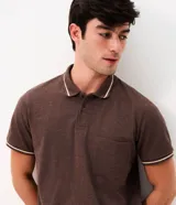 Remera polo masculina de algodón piqué color marrón, con cuello y puños acanalados en tono contrastante, cierre frontal con botones y bolsillo aplicado en el pecho.